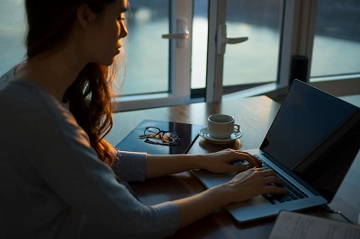 Photograph of a woman working on a laptop at twilight.